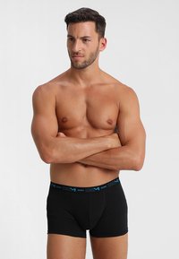 Mustat boxer-uutuudet, joissa on kontrastivärinen sininen vyötärö, jossa on brändin nimi. Sileä tekstuuri, muotoilultaan tiukka. Mallina toimii miesmalli.