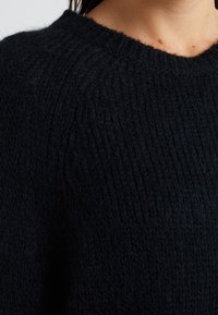 Maglione lavorato a maglia di un blu navy scuro con una texture a coste e colletto a girocollo. Materiale in misto lana, caratterizzato da un aspetto morbido e caldo.
