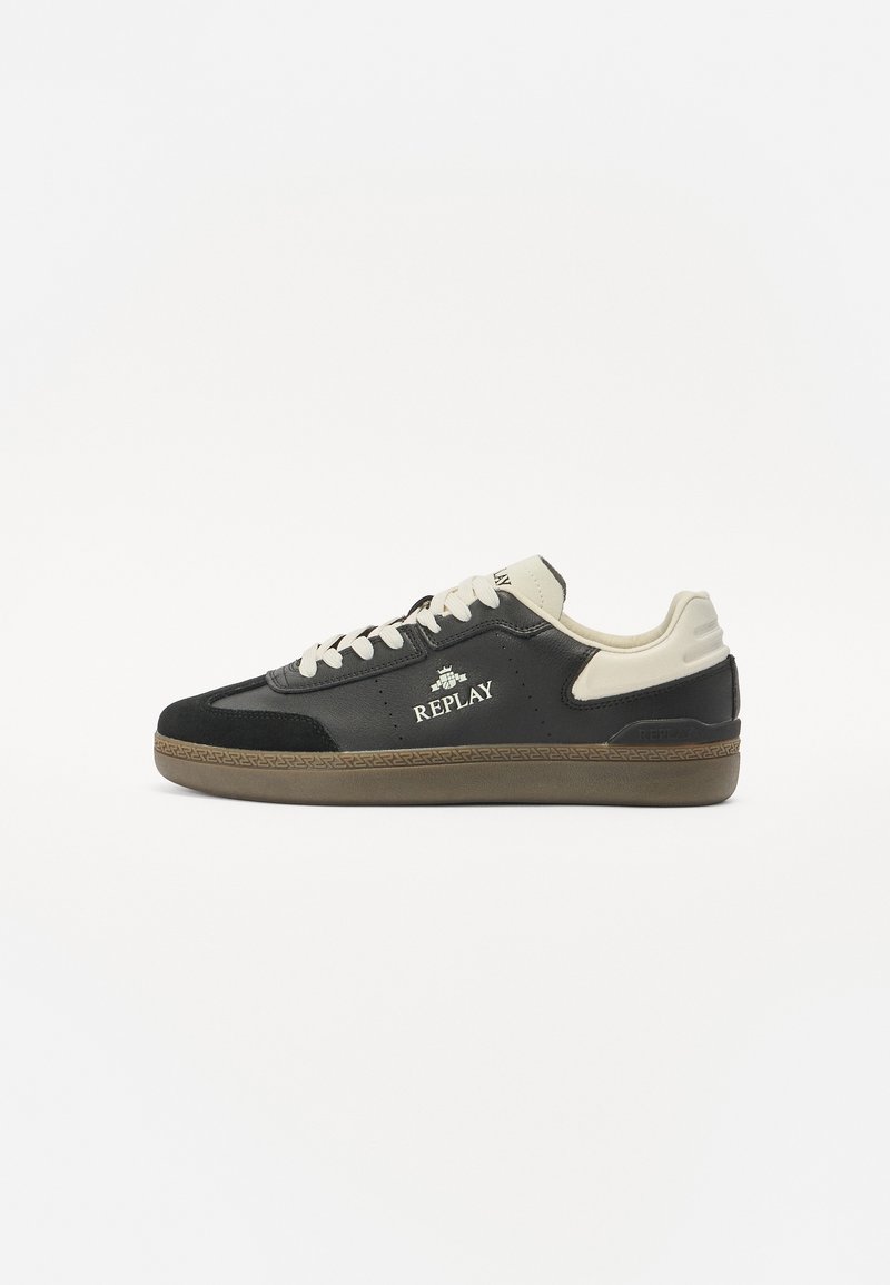 Schwarze und beige Sneakers mit einem Obermaterial aus Leder und Wildleder, ausgestattet mit reflektierenden Akzenten, Schnürsenkeln und einer Gummisohle. Logo an der Seite angebracht.