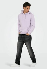 Levandų spalvos džemperis su kišene priekyje ir raišteliais, derinamas su tamsiai pilkomis džinsais ir baltais sportbačiais. Kasdienis, laisvo kirpimo stilius.