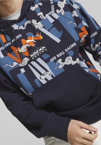 Felpa navy con stampa grafica che presenta accenti rossi, blu e bianchi. Mostra il logo "Red Bull Racing" e disegni astratti. Tessuto morbido.