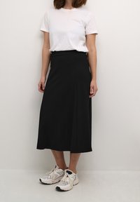 Mustat nilkkapituiset hameet, joissa on sileä pinta ja A-linjainen siluetti, yhdistettynä valkoiseen t-paitaan ja urheilukenkiin.