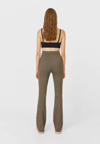 Pantalons évasés dans un motif tartan marron avec une finition texturée, taille haute et jambes longues. Portés avec un haut noir, vus de l'arrière.