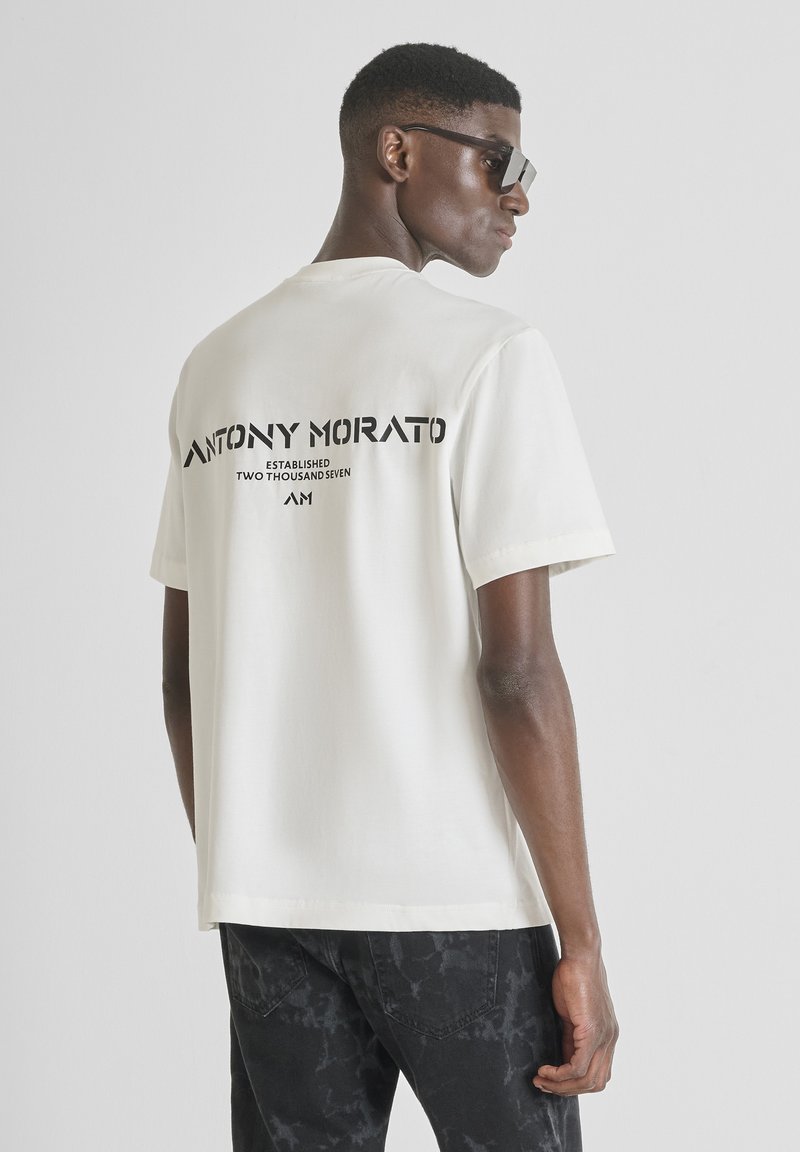 Camiseta de algodón crema de manga corta con un audaz estampado gráfico negro en la parte posterior, corte estándar y textura suave.