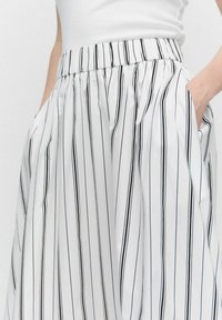 Jupe plissée blanche avec de fines rayures noires, taille élastique et poches latérales pour plus de fonctionnalité. Texture lisse et design décontracté.