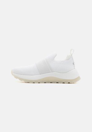 Biały sneaker wsuwany z dzianą cholewką, elastycznym paskiem nad śródstopiem, pętelką na pięcie i masywną beżową gumową podeszwą.