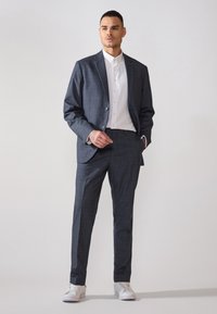 Completo checked blu scuro con giacca su misura e pantaloni slim-fit, abbinato a una camicia bianca e sneakers bianche.