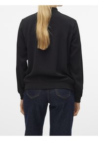 Sweat-shirt noir à manches longues avec ourlet côtelé, associé à un jean denim bleu foncé avec un design distinctif sur la poche arrière.