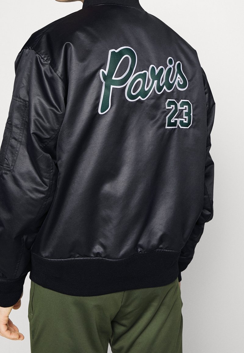 Black satin bomber jacket featuring "Paris" and "23" in green and white embroidery on the back, with ribbed cuffs and waistband.