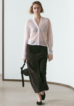 Hellrosa, durchsichtige, zum Knöpfen geeignete Strickjacke mit langen Ärmeln, kombiniert mit einem dunkelbraunen, knöchellangen, strukturierten Rock und schwarzen Ballerinas.