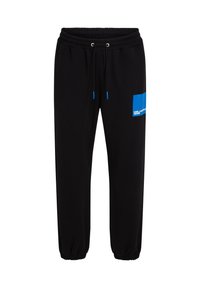 Schwarze Sweatpants mit einem elastischen Bund, kontrastierenden blauen Kordeln und einem blauen Grafikpatch mit Text auf dem linken Oberschenkel.