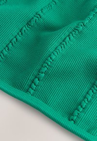 Tekstuuriga soonik kangas erkrohelises värvitoonis, millel on dekoratiivne õmblus ning pehme ja elastne viimistlus. Servad on korralikult alla lõigatud.