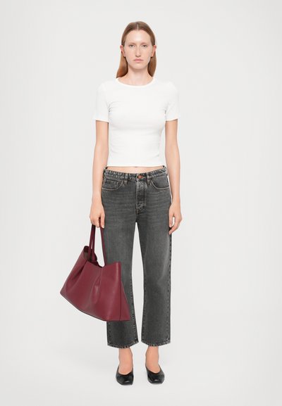 Geantă de tote din piele bordeaux, cu o textură netedă, deschidere largă și mânere scurte. Modelul poartă o cămașă alba, ajustată și blugi gri cu talie înaltă.