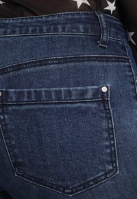 Tmavozelené džíny z denimu s klasickým designem, obsahující zadní kapsu a jemné švy po obvodu pasu.