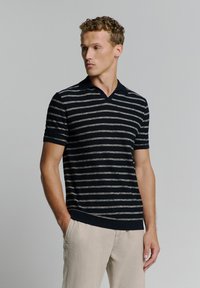 Marineblauwe polo met korte mouwen met lichtgrijze horizontale strepen, met een V-hals ontwerp en een ribgebreide onderrand. Zachte gebreide textuur.