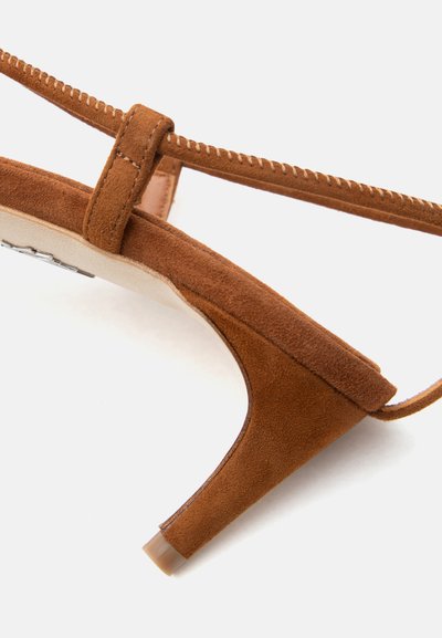 Sandale à talon kitten en daim marron avec une fine bride de cheville cousue et une semelle beige visible sur un fond blanc.