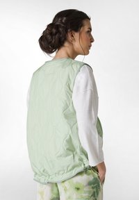 Gestepptes grünes Weste mit glatter Textur, rundem Halsausschnitt und gerafftem Saum. Trägt man über einem weißen Langarmoberteil mit lockerer Passform.