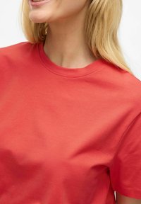 Rød bomulds t-shirt med en klassisk rund halsudskæring, glat tekstur og korte ærmer. Stoffet ser let og åndbart ud.