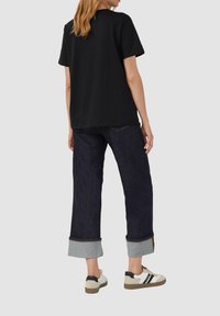 T-shirt noir à manches courtes associé à un jean large délavé foncé avec des ourlets roulés et des sneakers blanches avec des accents noirs.
