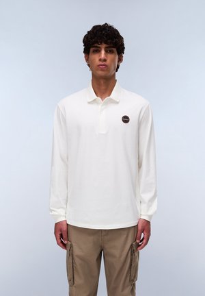 Camisa polo de manga larga blanca con cuello abotonado y un logo redondo en el lado izquierdo del pecho. Textura suave y corte regular.