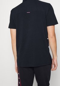 Musta lyhythihainen polo-paita, jossa on kaulus. Sisältää takatuuletuksen ja pienen väriltään poikkeavan tarran. Pehmeää puuvillamateriaalia.