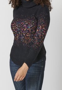 Černý rolák s vícebarevným flekatým vzorem na horní části; žebrované manžety a lem; měkký pletený materiál.