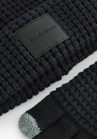 Svart stickade handskar med en vävd textur, en läderetikett med "ALLSAINTS" och en grå stickad spets på pekfingret.