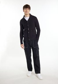Cardigan blu scuro con texture a coste, chiusura a bottoni e tasche frontali abbinato a pantaloni cargo neri con cuciture bianche e tasche.