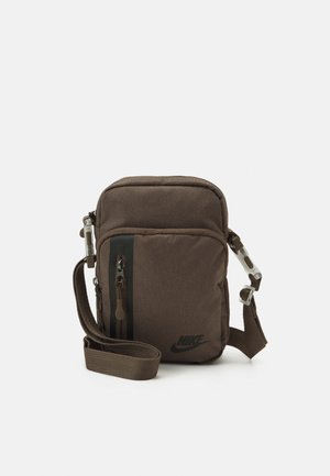 Petit sac bandoulière Nike marron foncé avec poche avant zippée, sangle réglable et logo noir sur fond uni.
