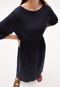 Laivastonsininen jersey-mekko, jossa on pyöreä pääntie, kyynärpään pituiset hihat ja joustava vyötärönauha, joka tarjoaa rentoa istuvuutta. Sileä pinta.