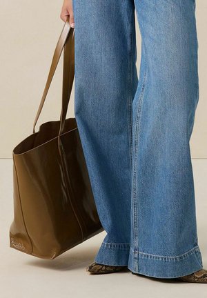 Bruine, glanzende strandtas met een gestructureerde vorm, uitgerust met lange handvatten, gecombineerd met lichtblauwe, wijde jeans en patronen op de schoenen.