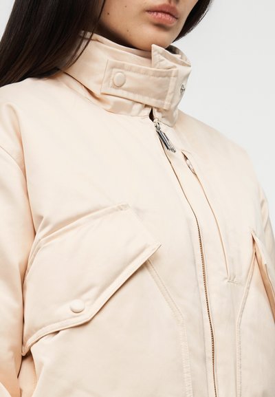 Svetloružová prešívaná bunda s vysokým golierom, dvoma veľkými prednými vreckami, zipsom so sťahovacou šnúrkou a hladkým povrchom.