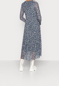 Długa, przezroczysta granatowa sukienka z białymi i jasnoniebieskimi plamkami, zwiewna spódnica w falbanki oraz okrągły dekolt. Noszona z białymi, masywnymi botkami.