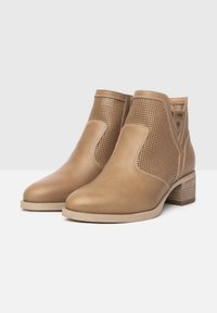 Tan leren enkelboots met geperforeerde zijpanelen, ronde neus en een gestapelde hak. Eenvoudige stiksels en een gladde textuur.
