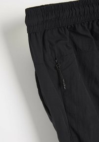 Czarne spodnie z elastycznym paskiem w pasie z sznurkiem, wykonane z teksturowanej, lekkiej tkaniny oraz posiadające boczną kieszeń na zamek.