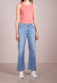 Top senza maniche color corallo, pantaloni a gamba larga alta vita di un blu chiaro, abbinati a sneakers bianche. Tessuto morbido, vestibilità rilassata e design semplice.