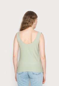 Top verde sem mangas com costas em forma de barco, feito de tecido macio, design ajustado e textura suave, combinado com jeans claros de cintura alta.