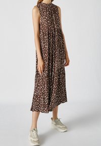 Brun ärmlös klänning med vitt prickmönster, rynkad halsringning och vågig design, ihopparad med ljusbeige sneakers.