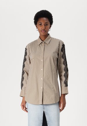 Striped skjorte med knapper i beige og svart med blonder detaljer på ermene. Har klassisk krage og avslappet passform.