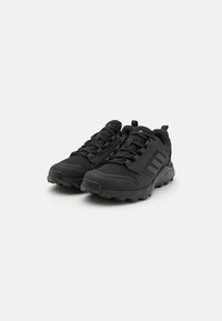 Black athletic shoes with a textured upper and rubber sole, featuring a lace-up design and three diagonal stripes on the side.