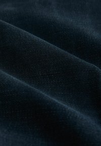 Tumed sinine tekstuuriga kangas, mille peen kudum on nähtav, esitades siledat pinda ja pehmet langevust, püüdes valguse pehmel moel voldikute kohal.