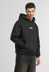 Sudadera negra de tejido suave con bolsillo tipo canguro y texto blanco "Piensa Distinto". Diseño sencillo con puños y dobladillo acanalados.