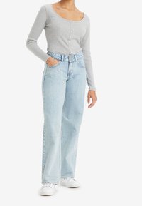 Grå ribbad långärmad topp med knappdetalj, ihopparad med högmidjade ljusblå vida jeans och vita sneakers.