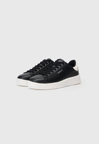 Black leather sneakers with a rounded shape, white rubber sole, and black laces. Features a contrasting heel tab and logo detail on the side.
