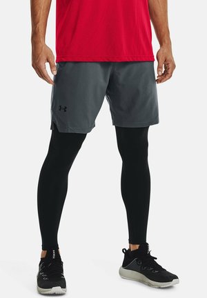 Grijze sportshorts gecombineerd met zwarte compressieleggings, een rode vochtafvoerende shirt en zwarte sneakers met grijze accenten.