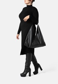 Abito lungo nero a maniche lunghe con orlo in pizzo, borsa hobo nera in pelle e stivali in pelle nera con tacco alto fino al ginocchio, tutti in una texture liscia.