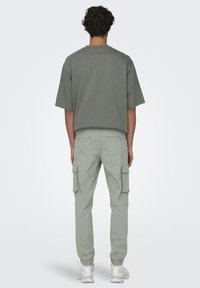 Oversized grijze katoenen t-shirt met verlaagde schouders, gecombineerd met lichtgroene cargo pants met zijzakken en elastische boorden.