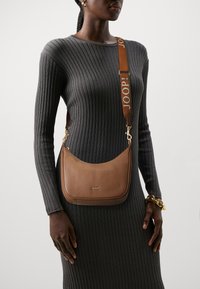 Borsa a spalla in pelle marrone dalla forma curva, logo impresso e tracolla regolabile a fantasia con la scritta "JOOP!" in colori a contrasto.