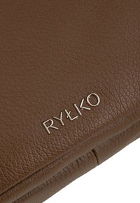 Bruine leren portemonnee met een gestructureerde afwerking en een gegraveerd zilveren "RYŁKO" logo. Compact ontwerp met zichtbare stikseldetails.