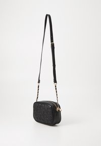 Černá kožená crossbody taška s embosovaným logem, obdélníkového tvaru, s nastavitelným popruhem, zlatými kovovými doplňky a zipovým uzávěrem.